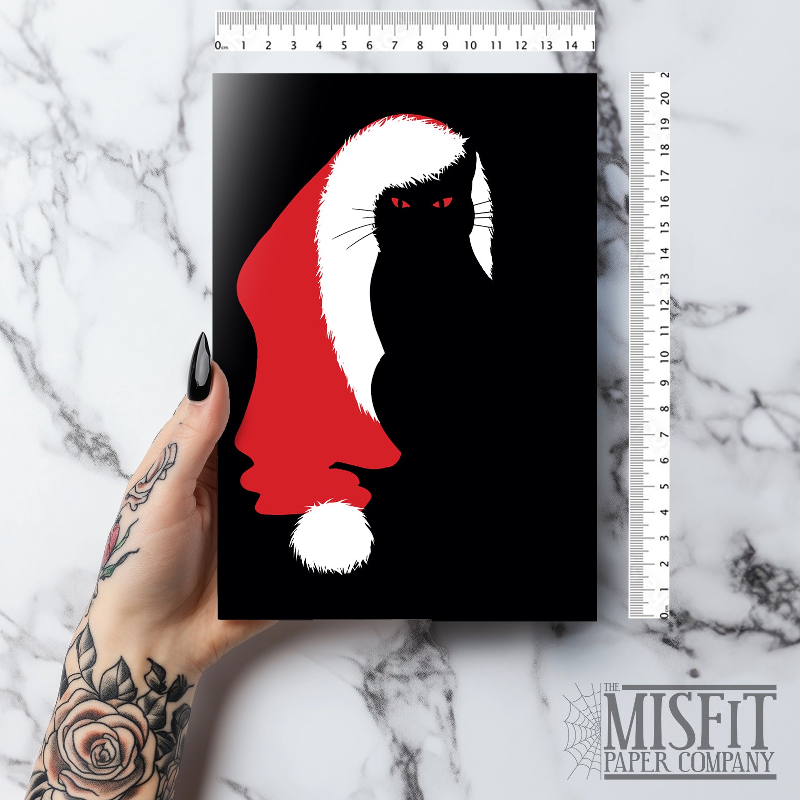 A5 glossy portrait Christmas card on black with minimalist red Santa hat and white trim forming space for a black cat silhouette with red eyes. Clean graphic style. Includes red envelope. Blank inside.
