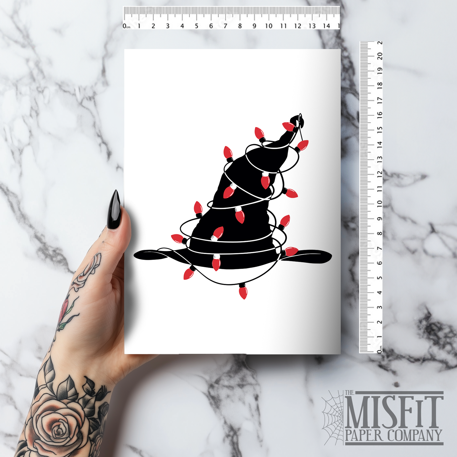 A5 glossy portrait Christmas card with minimalist black witch hat wrapped in red string lights on a white background. Clean graphic style. Includes red envelope. Blank inside.