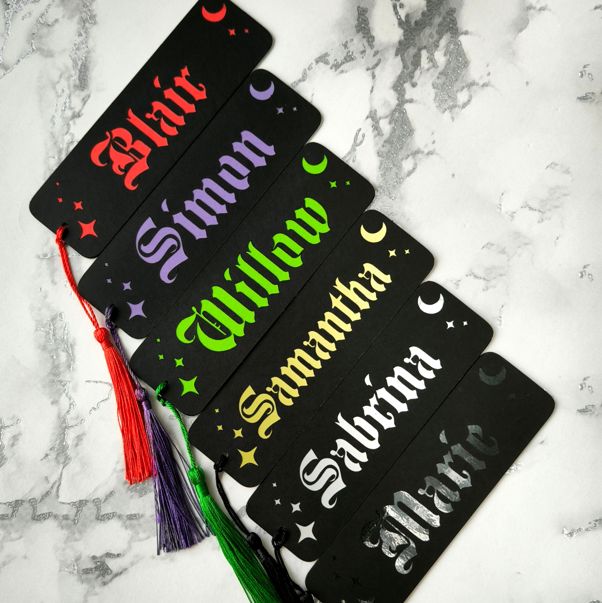 Custom gothic bookmarks with cutout names and celestial moon and star designs in red, purple, green, gold, and silver, with matching tassels