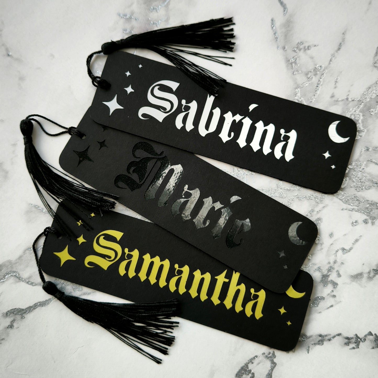 Custom gothic bookmarks with cutout names and celestial moon and star designs in red, purple, green, gold, and silver, with matching tassels