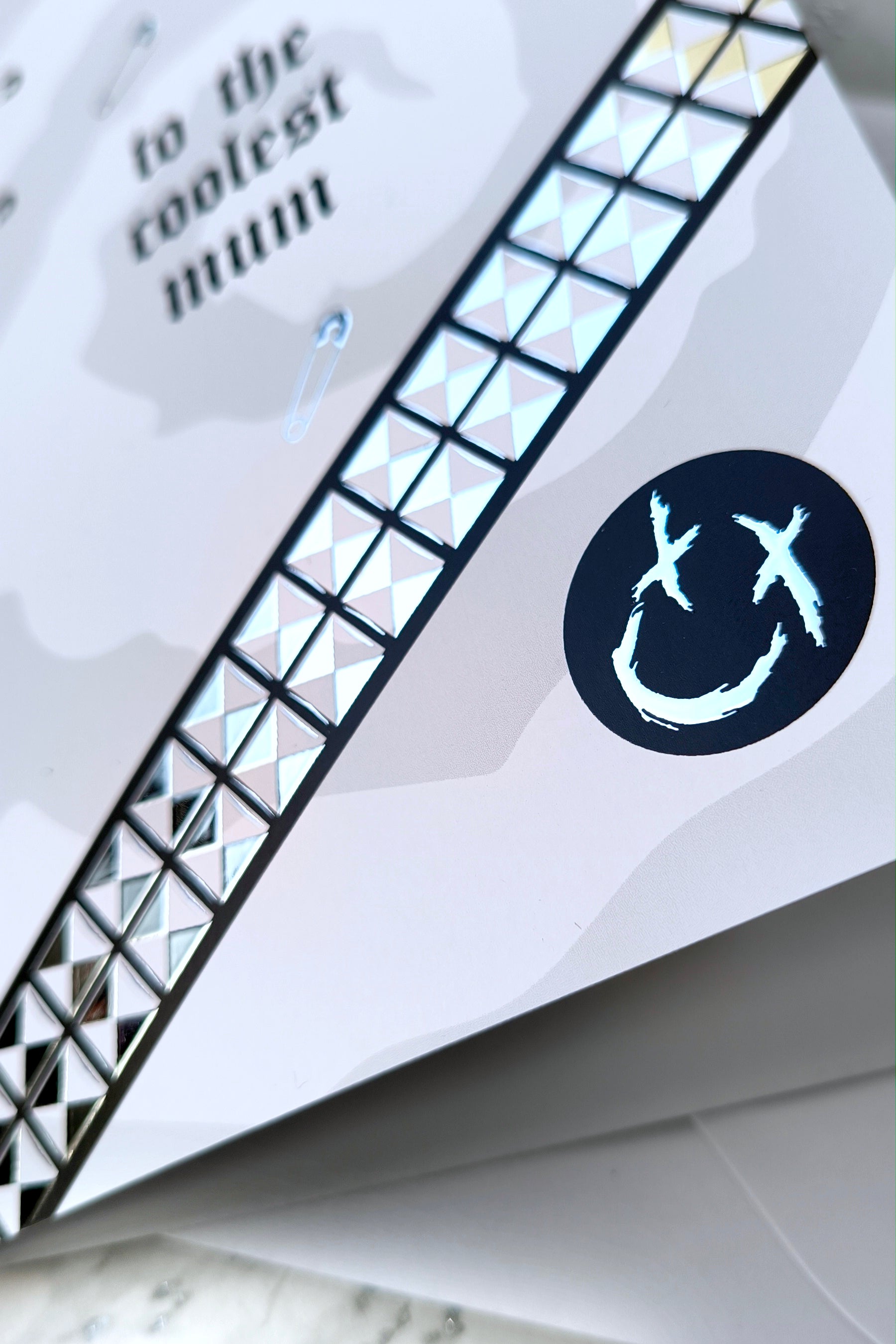 A5 greeting card reading “to the coolest mum” with gothic emo styling, featuring chrome stud belt graphic, safety pin details and a black smiley badge, paired with a white envelope.