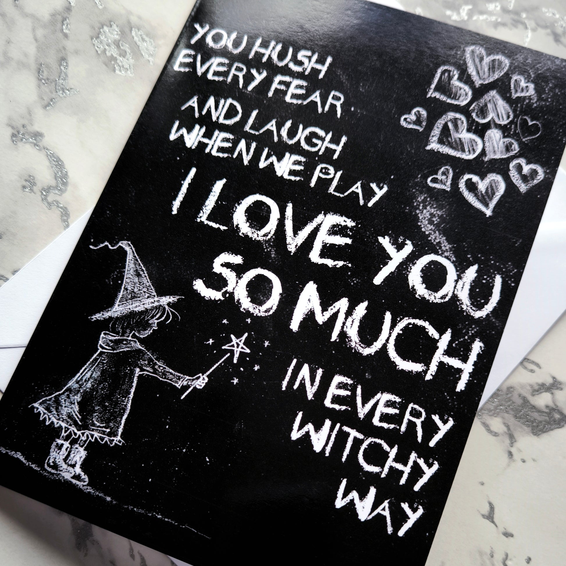 A black A5 greeting card with a chalkboard-style background, featuring a hand-drawn witch illustration casting a spell with floating love hearts. A sweet rhyming poem is written in chalk-style lettering. The card reads Happy Mother's Day inside and comes with an envelope.