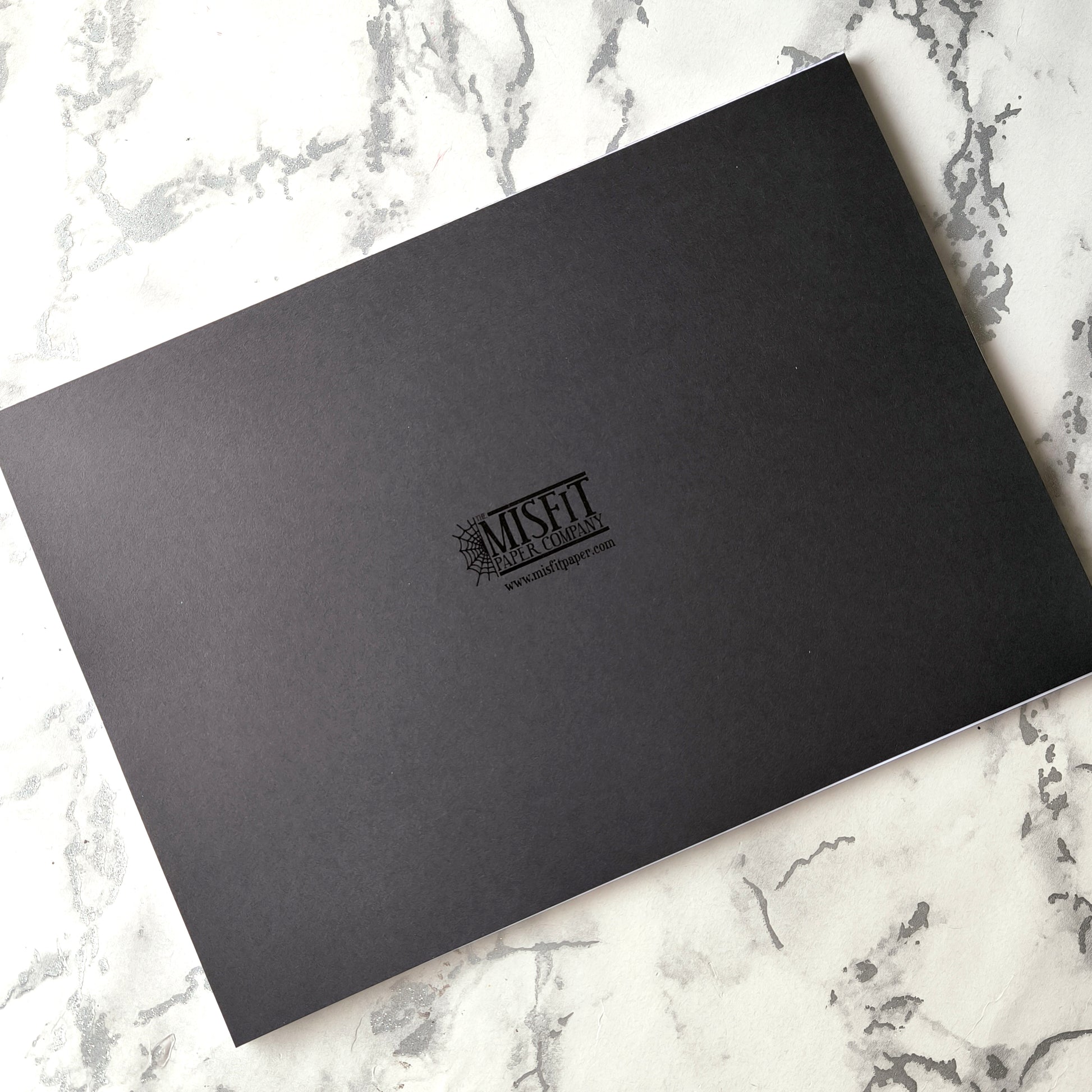 Undated weekly planner pad with black and white line-art frames and doodles. Blank boxes for each day, notes area, colouring-friendly layout. Desk pad style on smooth paper.