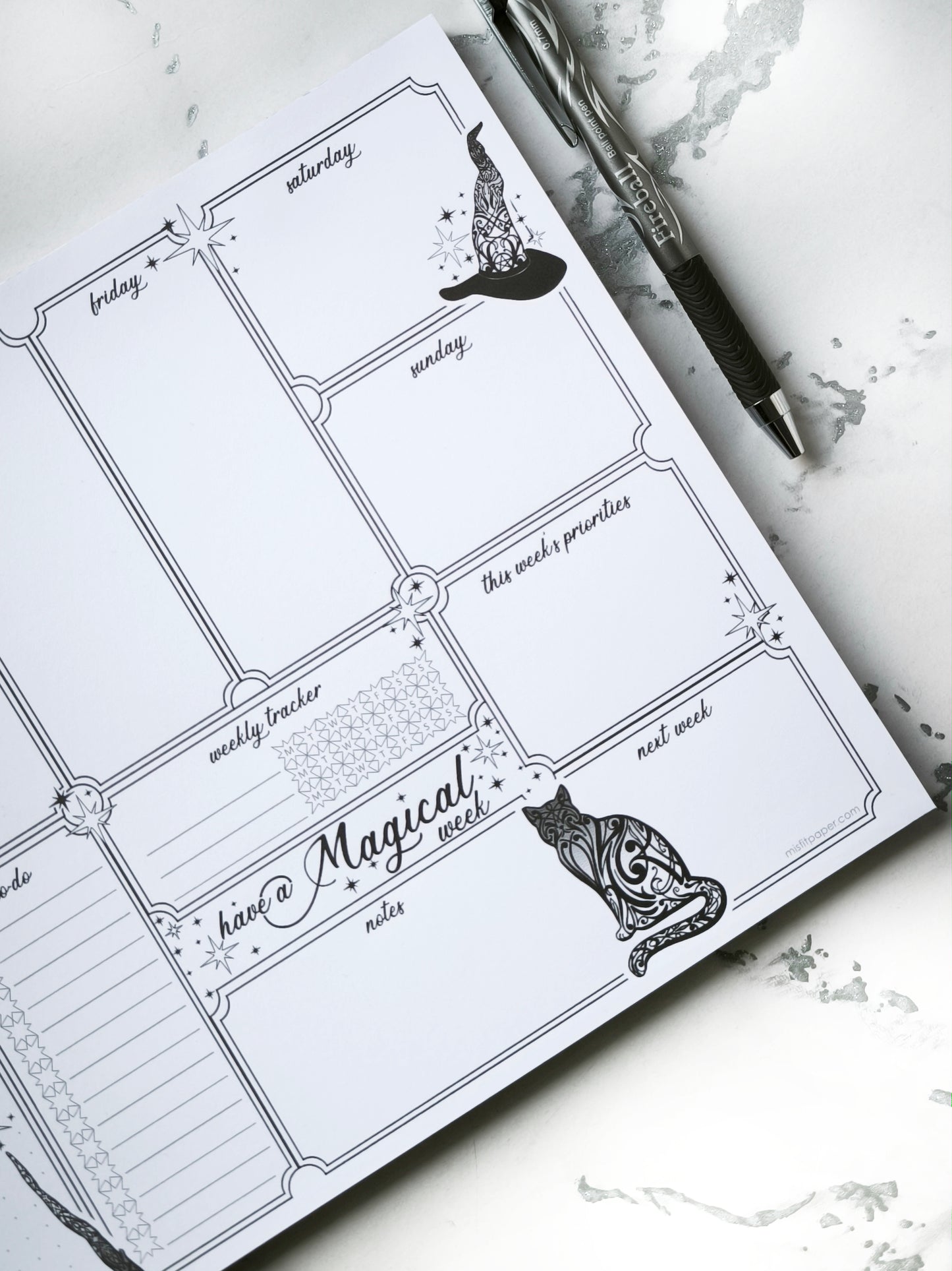 Undated weekly planner pad with black and white line-art frames and doodles. Blank boxes for each day, notes area, colouring-friendly layout. Desk pad style on smooth paper.
