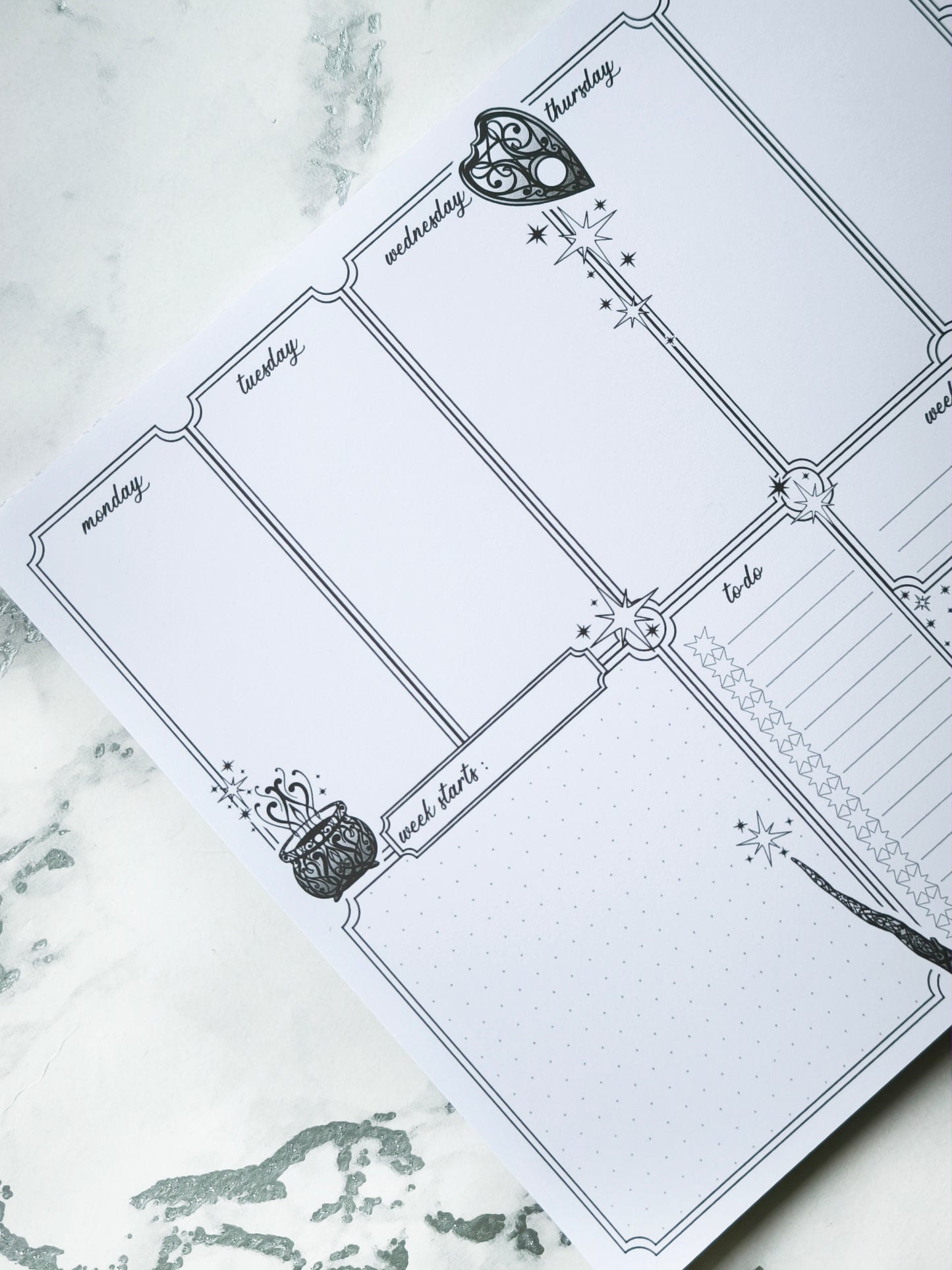 Undated weekly planner pad with black and white line-art frames and doodles. Blank boxes for each day, notes area, colouring-friendly layout. Desk pad style on smooth paper.