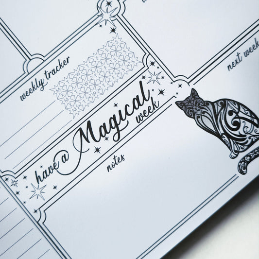 Undated weekly planner pad with black and white line-art frames and doodles. Blank boxes for each day, notes area, colouring-friendly layout. Desk pad style on smooth paper.