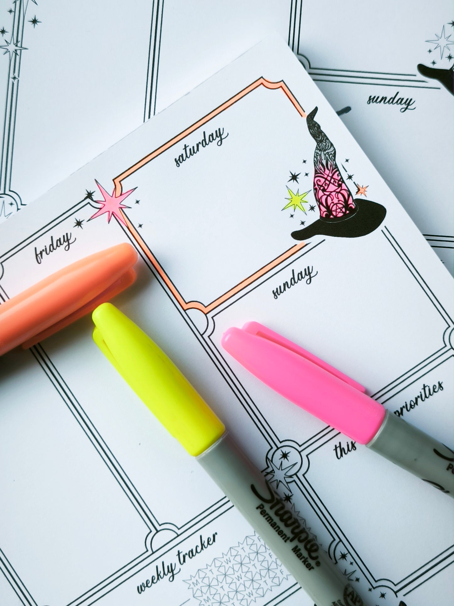 Undated weekly planner pad with black and white line-art frames and doodles. Blank boxes for each day, notes area, colouring-friendly layout. Desk pad style on smooth paper.