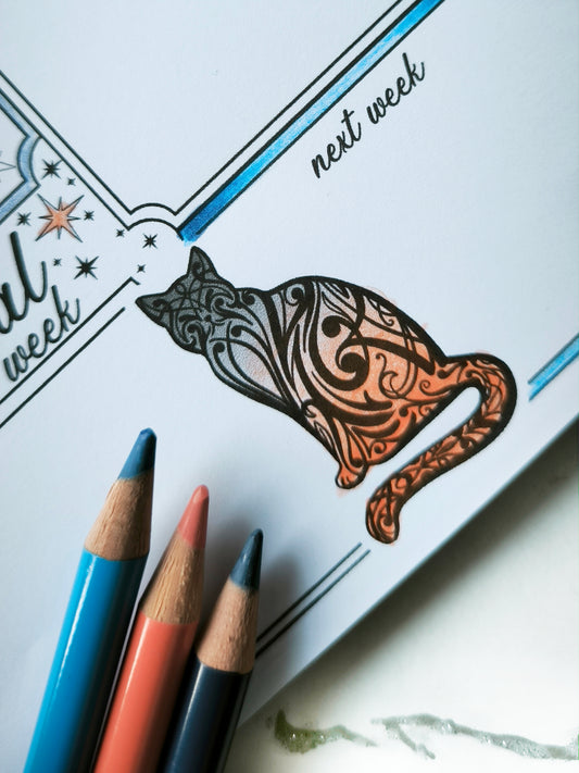 Undated weekly planner pad with black and white line-art frames and doodles. Blank boxes for each day, notes area, colouring-friendly layout. Desk pad style on smooth paper.