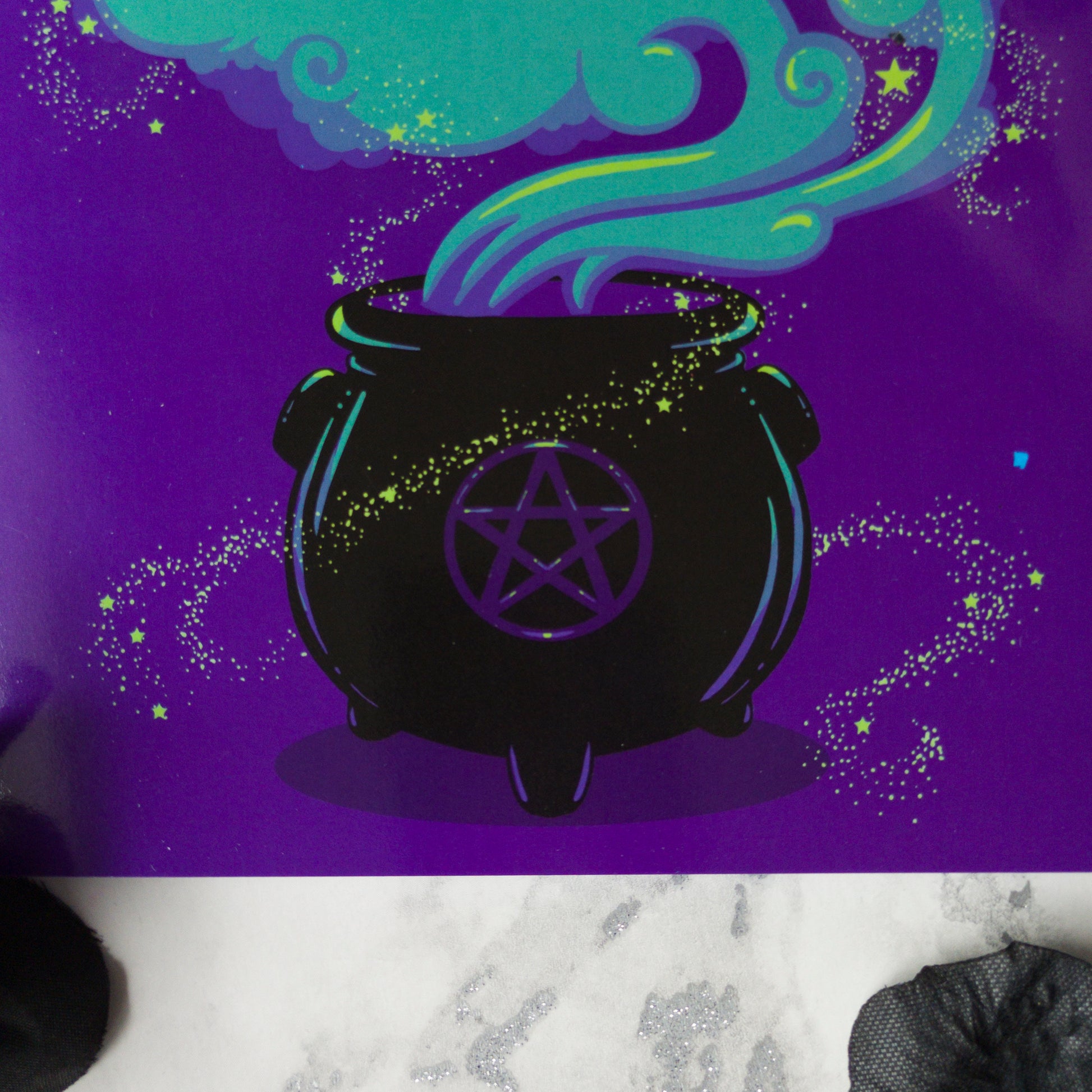 A large A5 greeting card in purple or pink, featuring a witchy cauldron illustration with billowing sparkling clouds and the words "Have a Magickal Mother’s Day." The inside has an illustration only (no text). Comes with an envelope included.