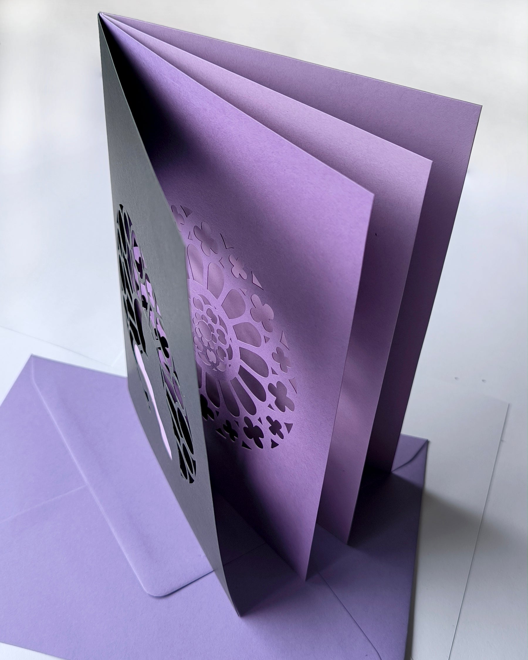 Handmade papercut greeting card, with a layered rose window in purple and black. Features a mother and baby silhouette in front of the gothic cathedral window design. Includes matching purple envelope.