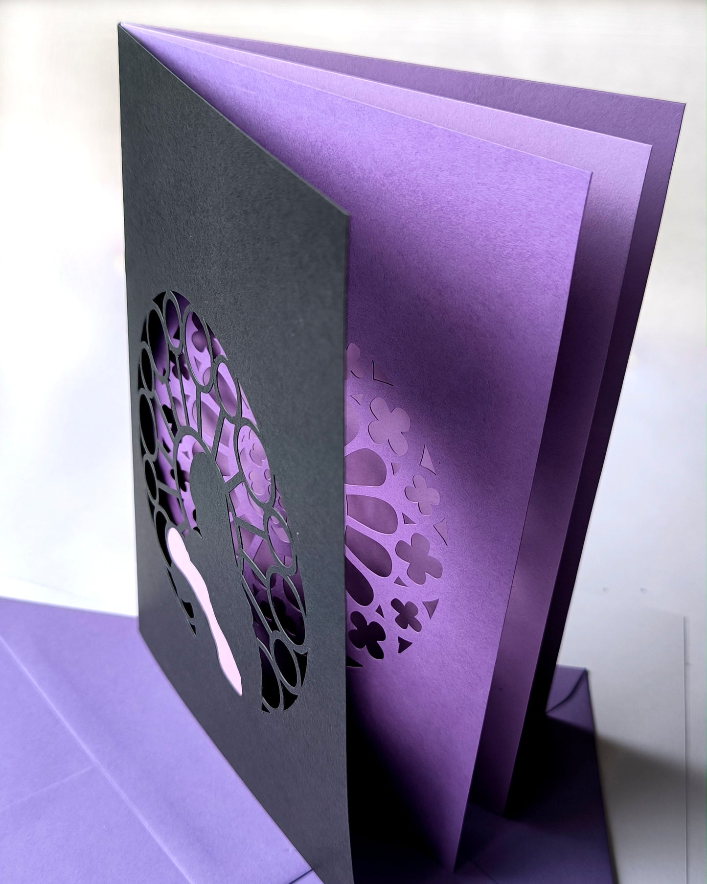 Handmade papercut greeting card, with a layered rose window in purple and black. Features a mother and baby silhouette in front of the gothic cathedral window design. Includes matching purple envelope.