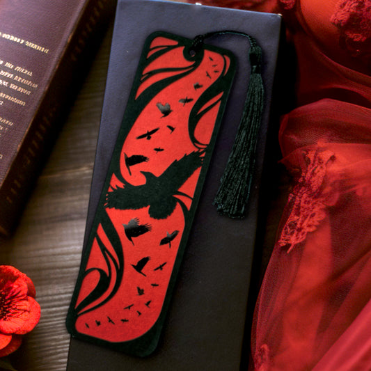 A handmade card bookmark. the black top layer is cut to a sweeping crow silhouette framed by flowing lines, set against a blood-red base scattered with glossy black-foiled crows in flight. Finished with a sleek black tassel.