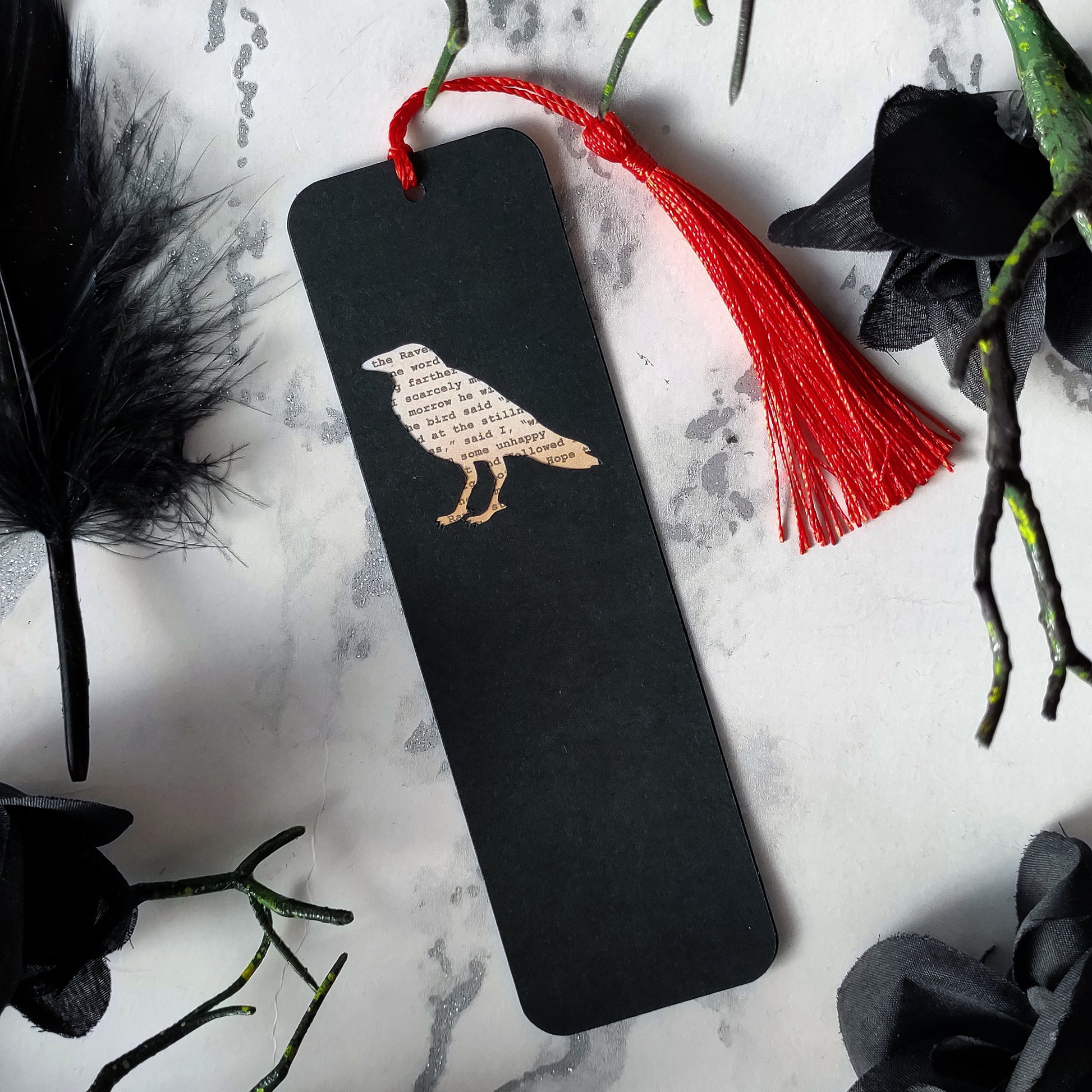 Handmade bookmark inspired by Edgar Allan Poe's poem The Raven. A raven shape cut from on each side of black card reveals a yellowed and aged section of text from the iconic horror classic, and is finished off with a silky red tassel.