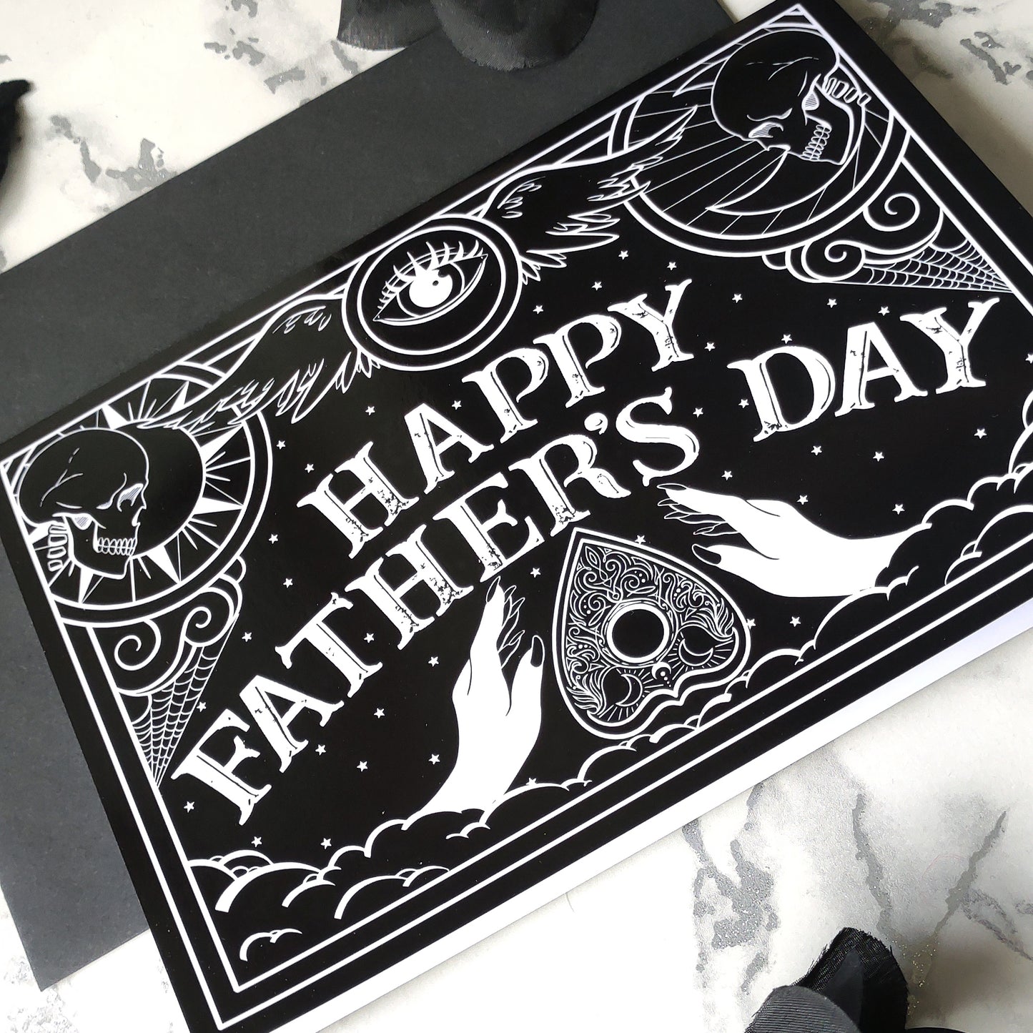 A5 gothic Father’s Day card featuring black and white Ouija board design with ornate “Happy Father’s Day” lettering and planchette detail. Blank inside with envelope. Ideal for witchy, spooky, or alternative dads.