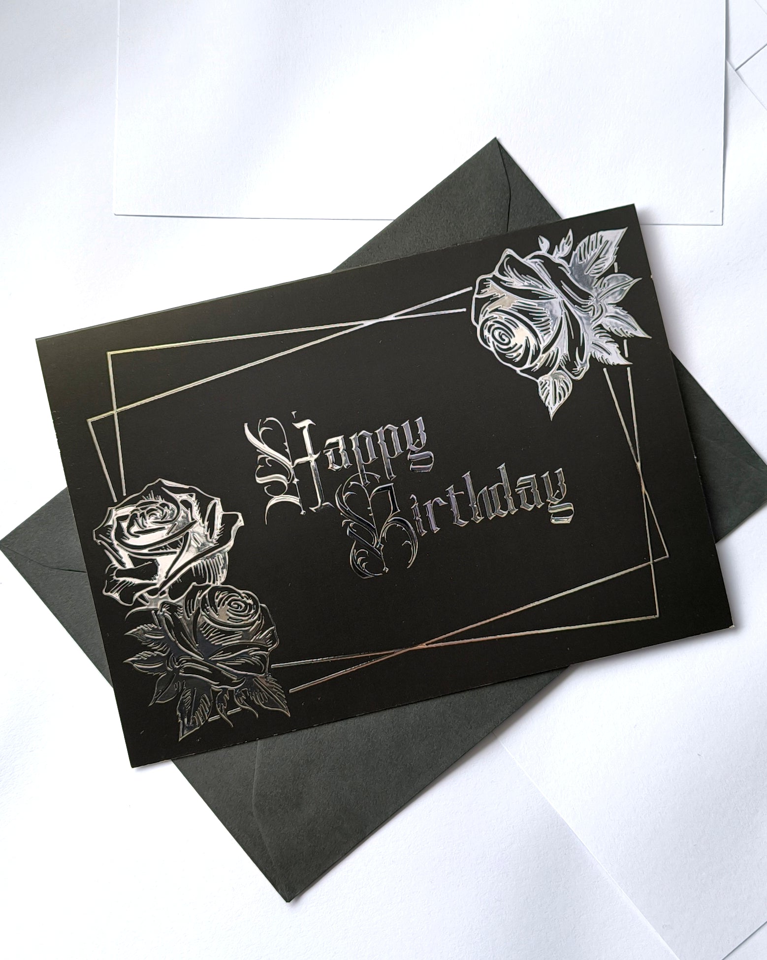A smooth black card with raised silver chrome detailing. Silver gothic text reads Happy Birthday, surrounded by a silver rectangular frame and silver roses in two corners.