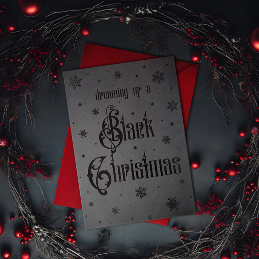 A5 handmade black Christmas card with black foil snowflakes and gothic lettering reading “Dreaming of a Black Christmas”. Portrait format on smooth black card with red interior. Includes red envelope. Blank inside.