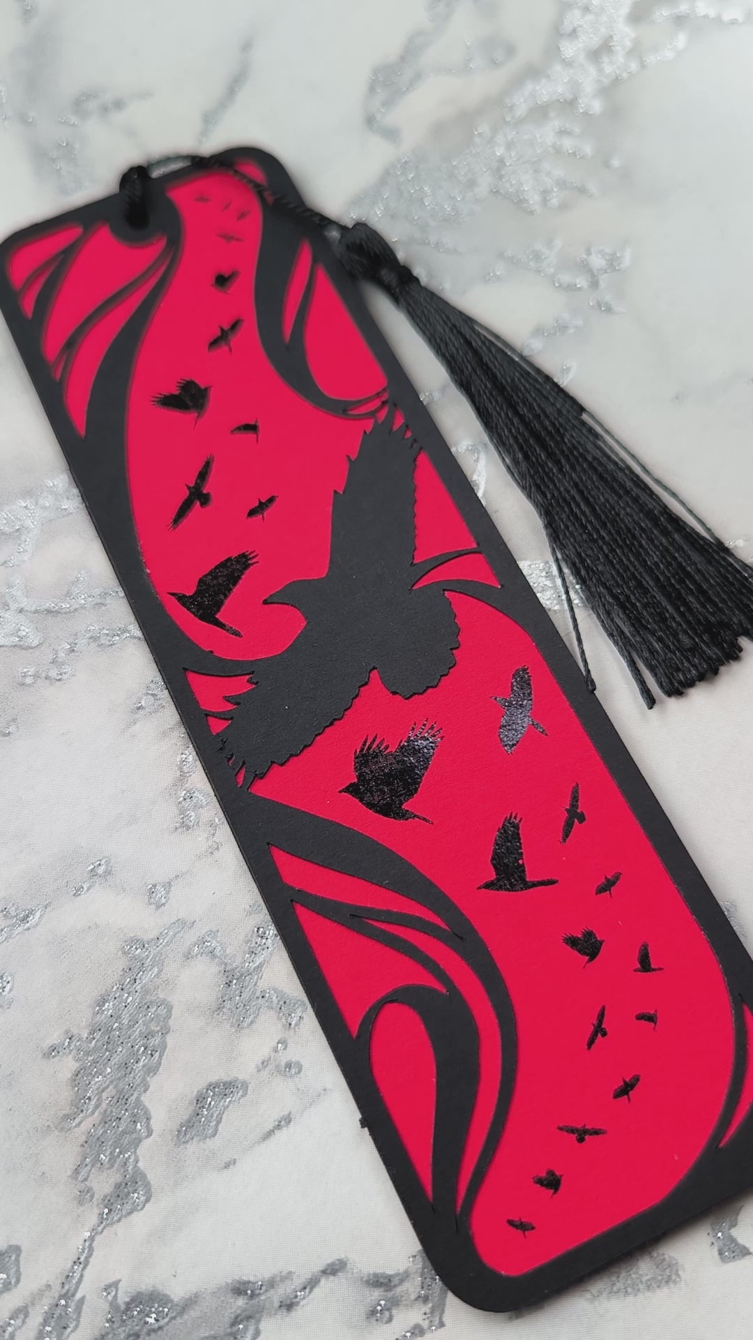 A handmade card bookmark. the black top layer is cut to a sweeping crow silhouette framed by flowing lines, set against a blood-red base scattered with glossy black-foiled crows in flight. Finished with a sleek black tassel.