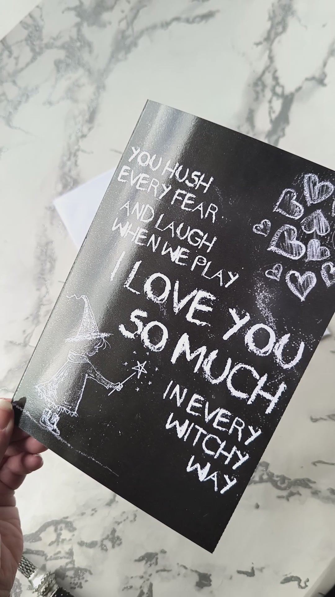 A black A5 greeting card with a chalkboard-style background, featuring a hand-drawn witch illustration casting a spell with floating love hearts. A sweet rhyming poem is written in chalk-style lettering. The card reads Happy Mother's Day inside and comes with an envelope.
